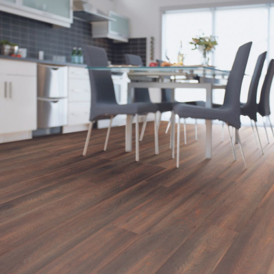 A contemporary dining and kitchen area with dark brown wood-look flooring, a glass dining table, and white kitchen cabinets in the background.